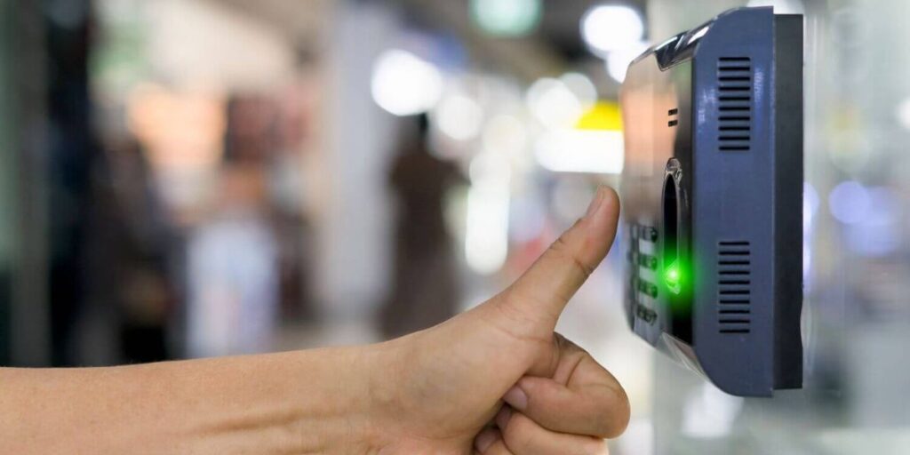 Person using fingerprint scanner on biometric attendance device in a modern office environment.