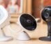 Three indoor wireless security cameras on a table: an Arlo, a Logi, and a Nest camera.