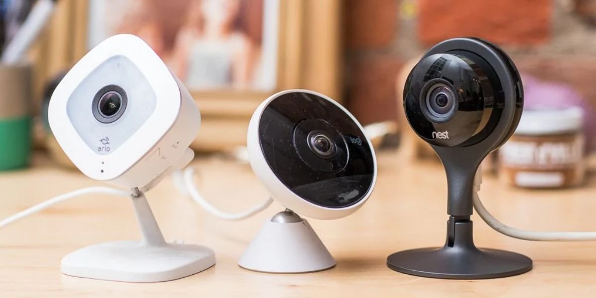 Three indoor wireless security cameras on a table: an Arlo, a Logi, and a Nest camera.