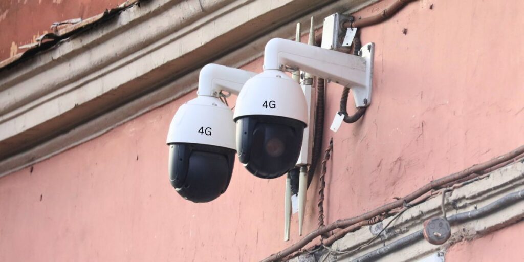 Two white and black 4G dome cameras are mounted side-by-side on a textured pink wall