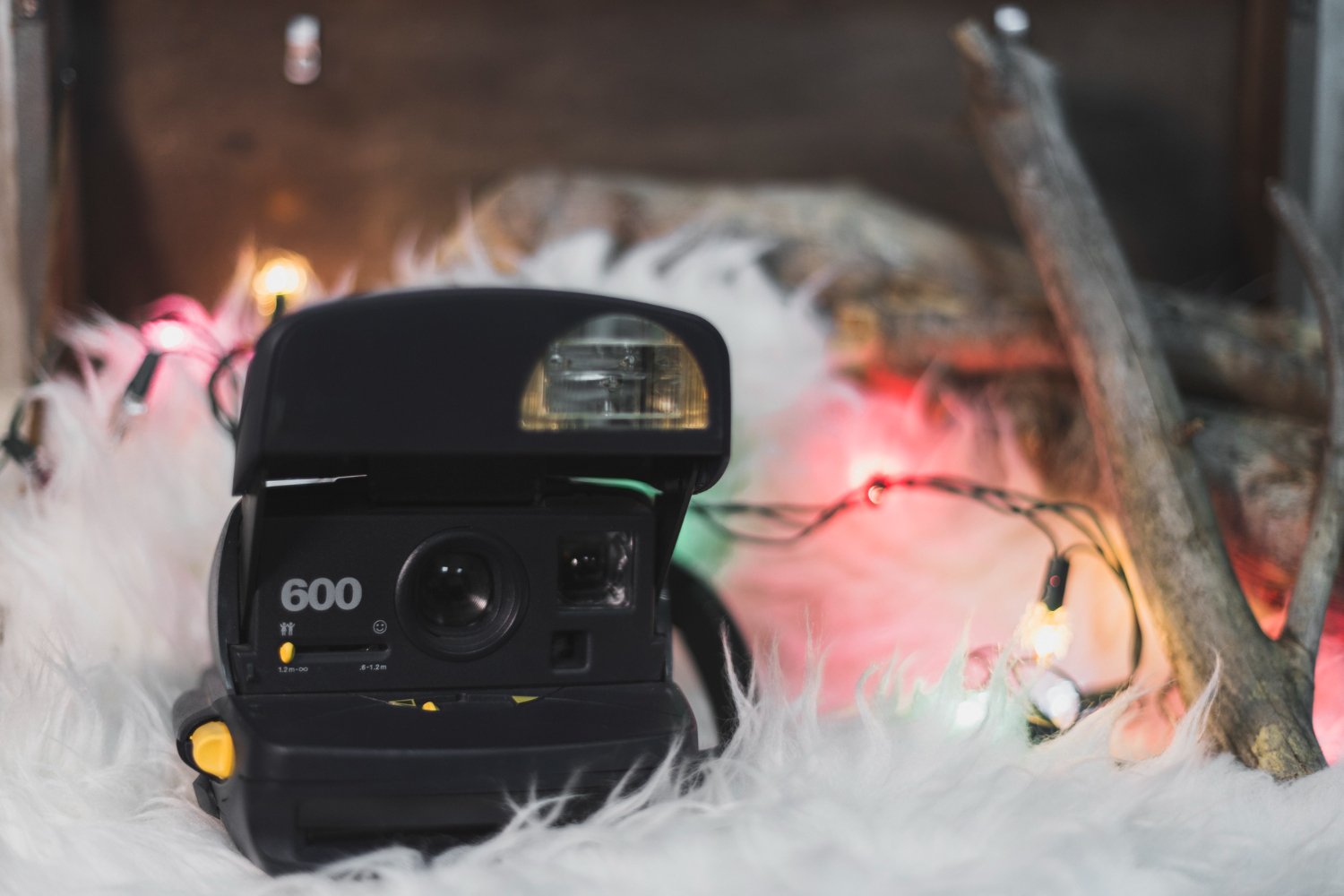 A vintage Polaroid 600 instant camera resting on white faux fur surrounded by string lights and wood