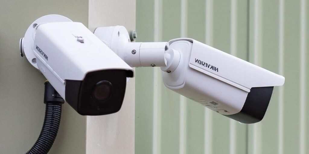 Two white bullet-style Hikvision security cameras mounted on an exterior corner with a black wire conduit