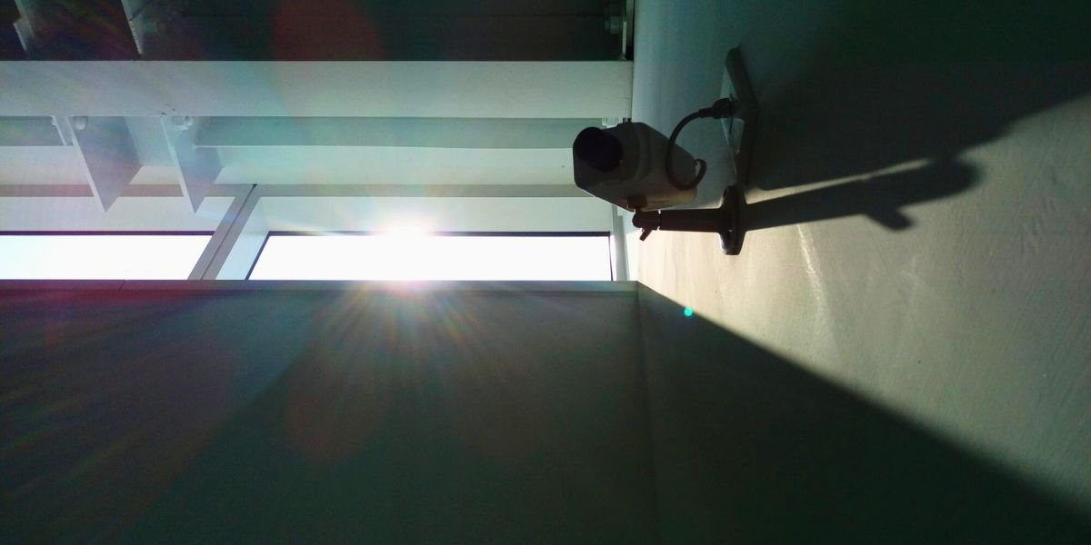 A security camera mounted on an indoor wall facing a window with bright, direct sunlight flare.