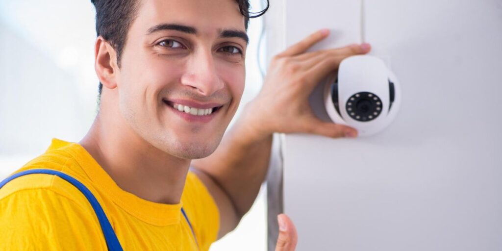 A man installs a white security camera on a wall next to an old, yellowed Canon CCTV camera