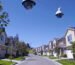 A wide-angle view of a suburban street with three large security cameras digitally edited to float in the clear sky.