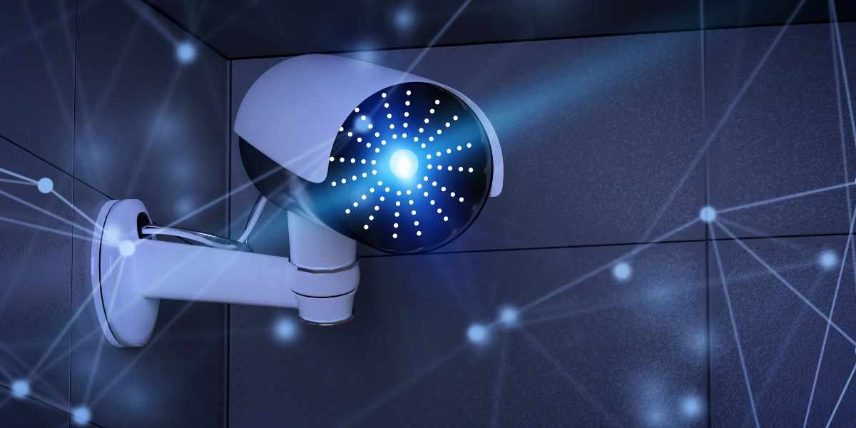 Modern white CCTV camera on a dark wall with a glowing blue lens
